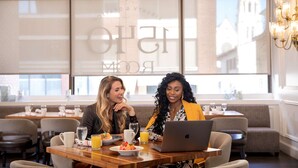A dining area with a large window, a laptop on the table, and a chandelier. - Walk to River Street | Pool. Dining + On-Site Bar (Savannah)