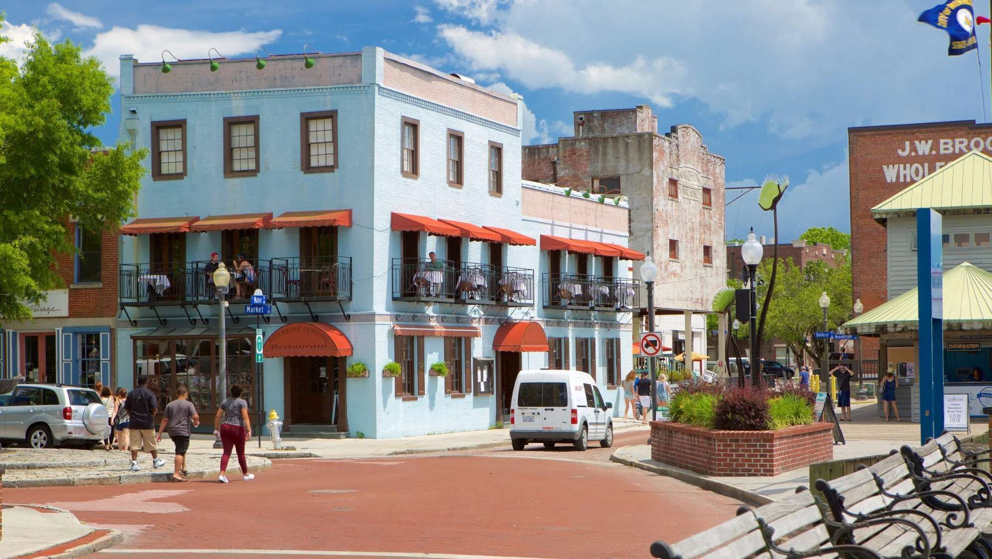 A street with a blue building with balconies, a white van, and a J.W. BROOKS WHOLE FOODS store.
