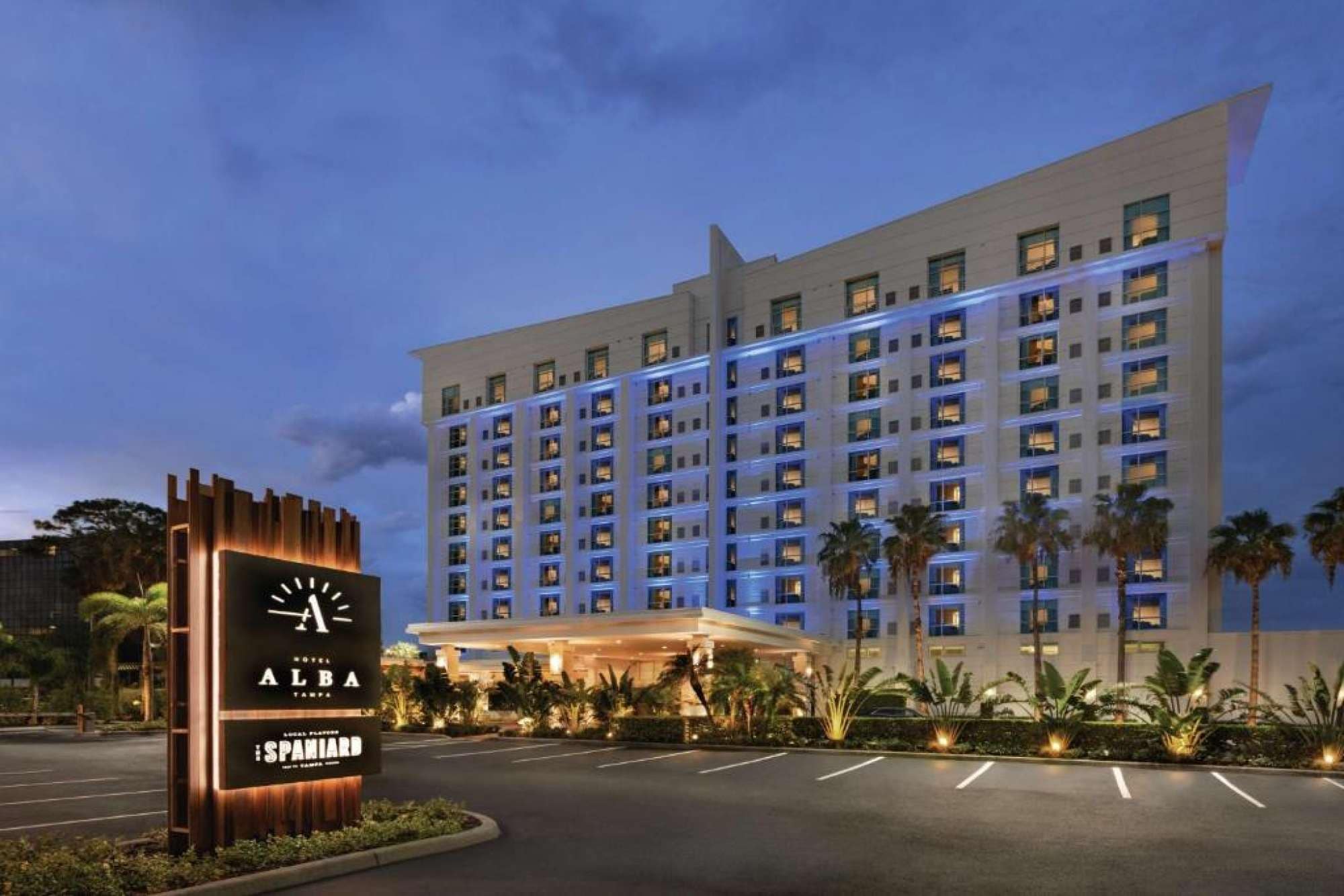A multi-story hotel with a modern facade, a well-lit entrance, and a landscaped area with palm trees.