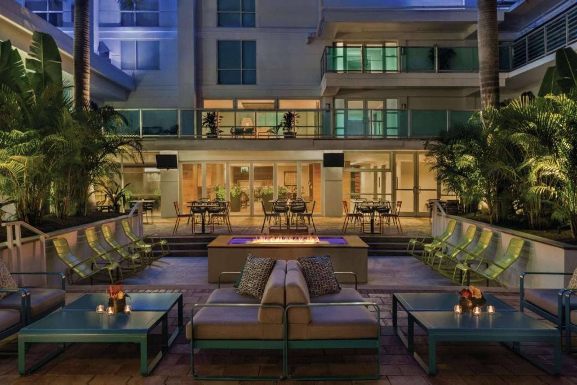 A modern outdoor lounge area with a fire feature, seating, and a view of the building's interior.