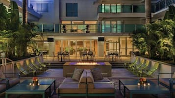 A modern outdoor lounge area with a fire feature, seating, and a view of the building's interior.