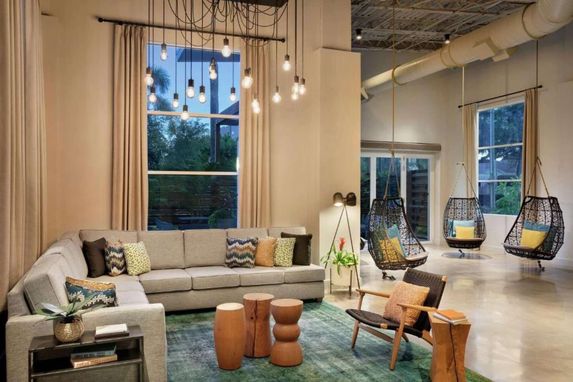 A modern living room with a sofa, side tables, hanging chairs, and large windows.