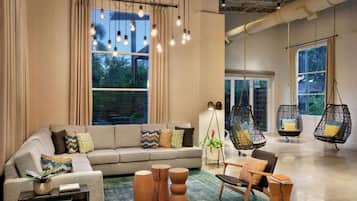 A modern living room with a sofa, side tables, hanging chairs, and large windows.
