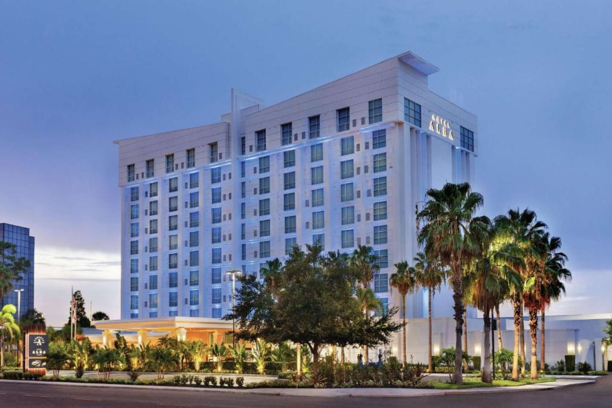 Een meerlaags hotel met een moderne gevel, voorzien van een opvallende entree met een overdekt gedeelte en palmbomen op de voorgrond.