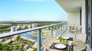 Un balcon avec une table dressée pour le petit-déjeuner, d’où l’on peut admirer un panorama sur la ville et un plan d’eau.