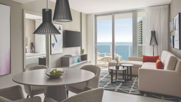 A modern living room with a round dining table, a sofa, and a balcony with a view of the sea. - Direct Ocean Views + Rooftop Pool. Bar. Tennis. (Hollywood)
