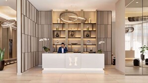 A modern reception area with a central desk, vertical shelving with decorative items, and a large circular chandelier. - Steps from Hollywood Beach + Rooftop Pool. Bar. (Hollywood)