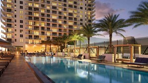 A hotel pool area with a large building in the background, lounge chairs, and palm trees. - Steps from Hollywood Beach + Rooftop Pool. Bar. (Hollywood)