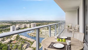 A balcony with a table set for two, overlooking a cityscape and a body of water. - Steps from Hollywood Beach + Rooftop Pool. Bar. (Hollywood)