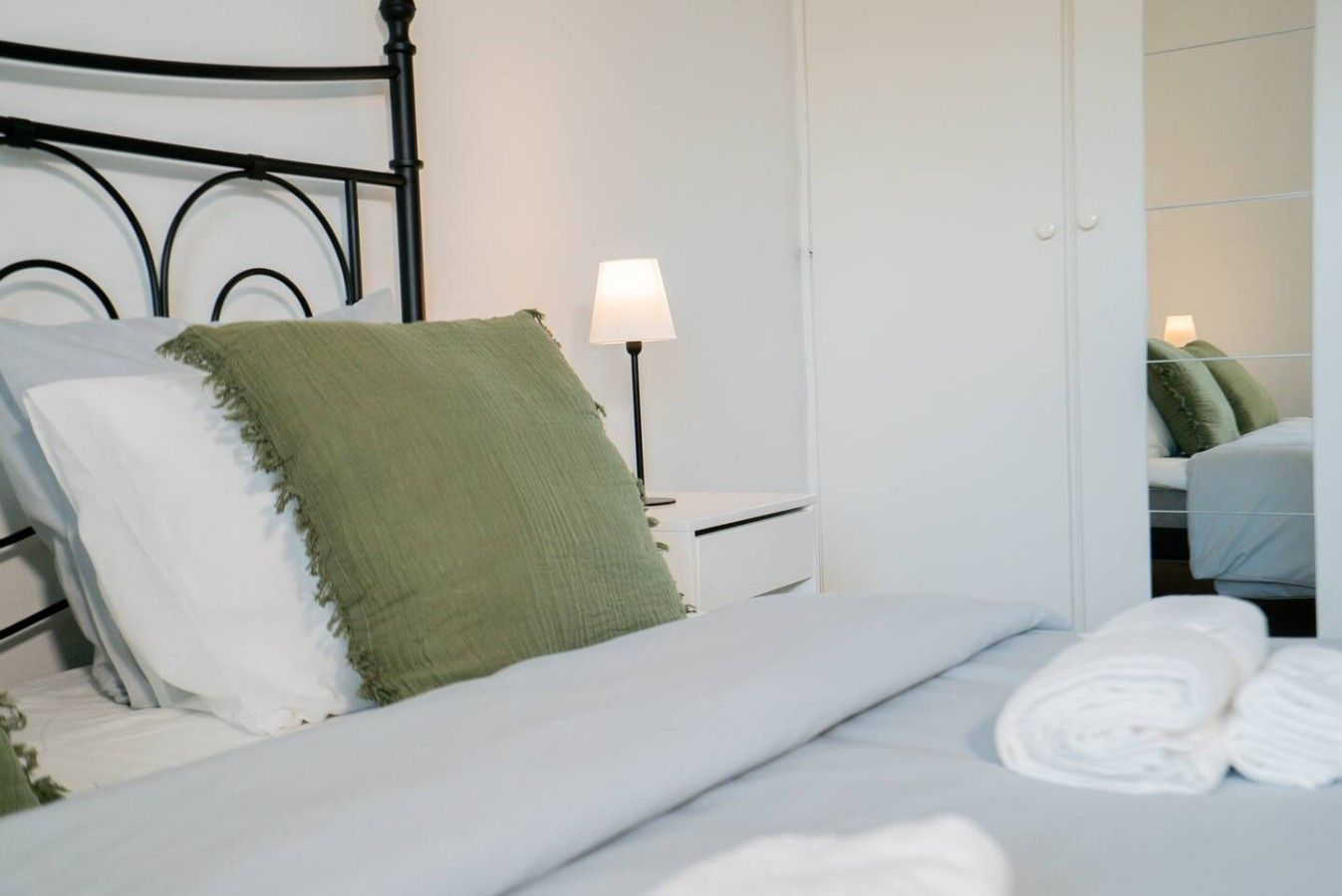 A neatly made bed with white and green pillows, a bedside lamp, and a white wardrobe in a hotel room.