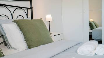 A neatly made bed with white and green pillows, a bedside lamp, and a white wardrobe in a hotel room.