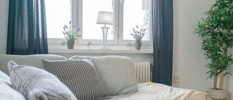 Una sala de estar con un sofá, dos plantas en macetas, una lámpara y una ventana con cortinas.
