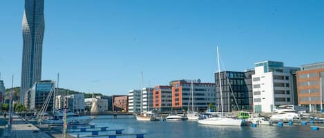 A marina with boats docked, a tall building, and a variety of other buildings in the background.