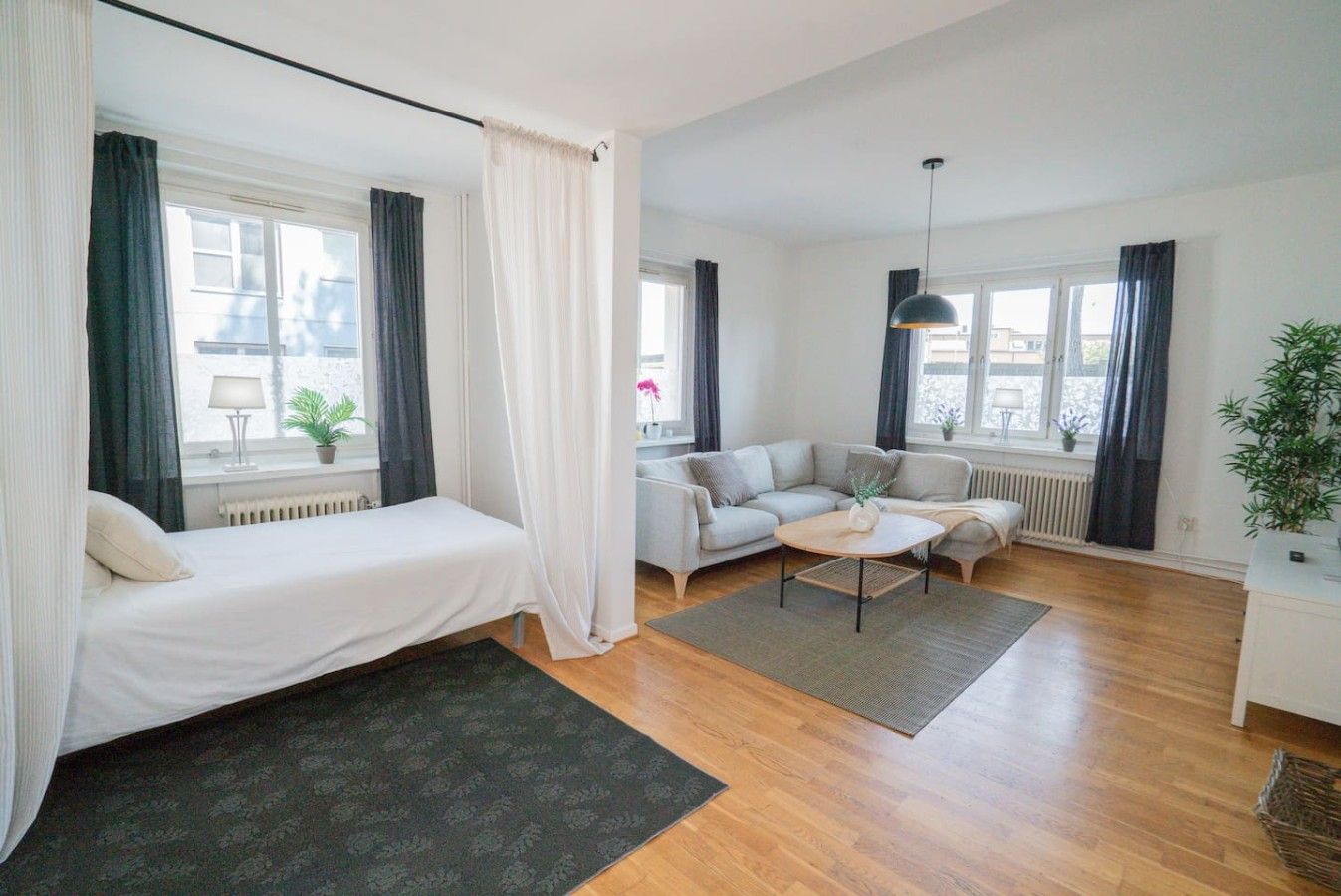A modern hotel room with a bed, a sofa, a coffee table, and a large window.