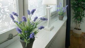 Ett fönster med utsikt över träd, en vit lampa och två krukväxter på en vit fönsterbräda.
