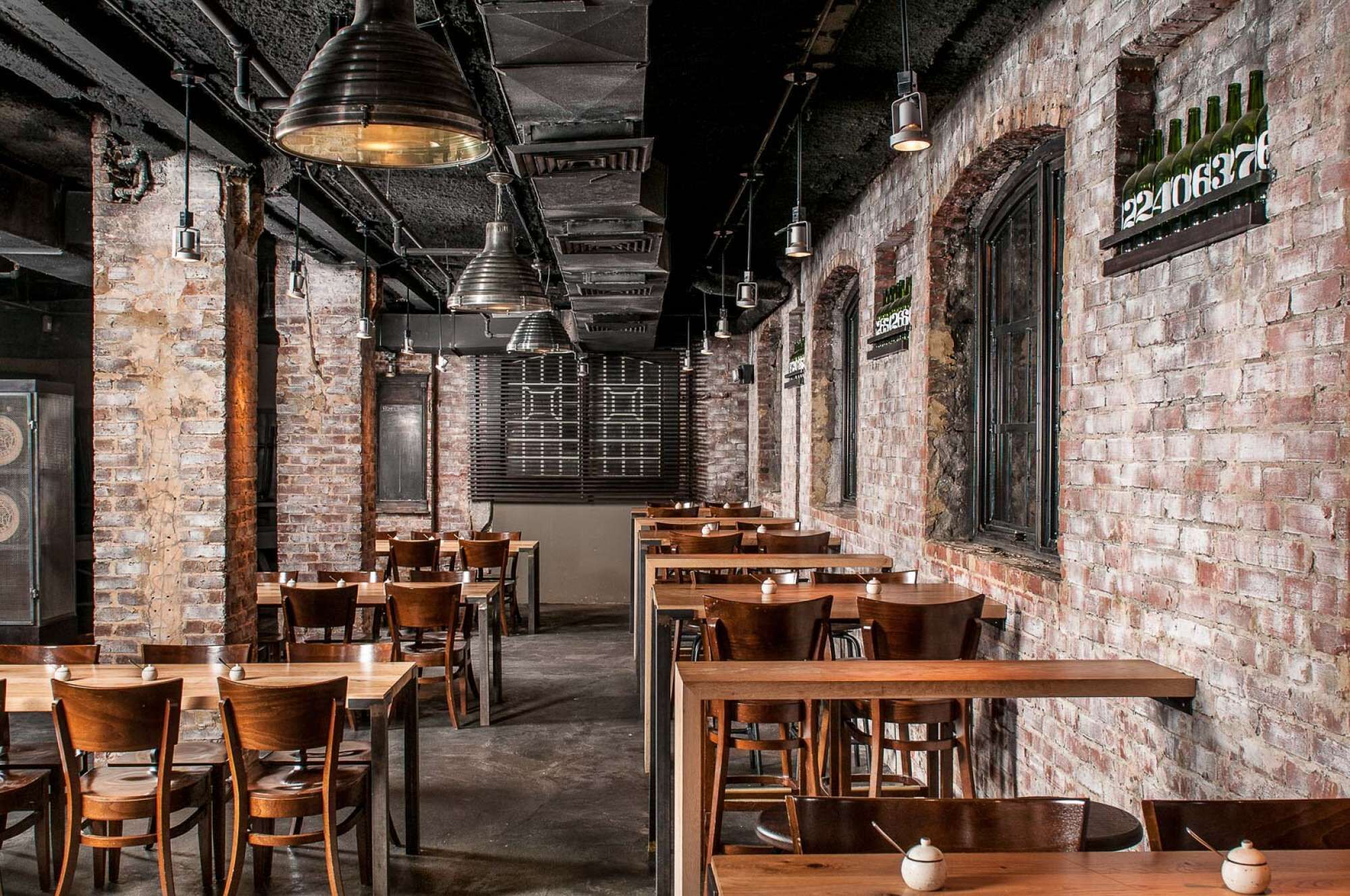 A restaurant interior with brick walls, exposed ceilings, and hanging pendant lights. Tables and chairs are arranged for dining.