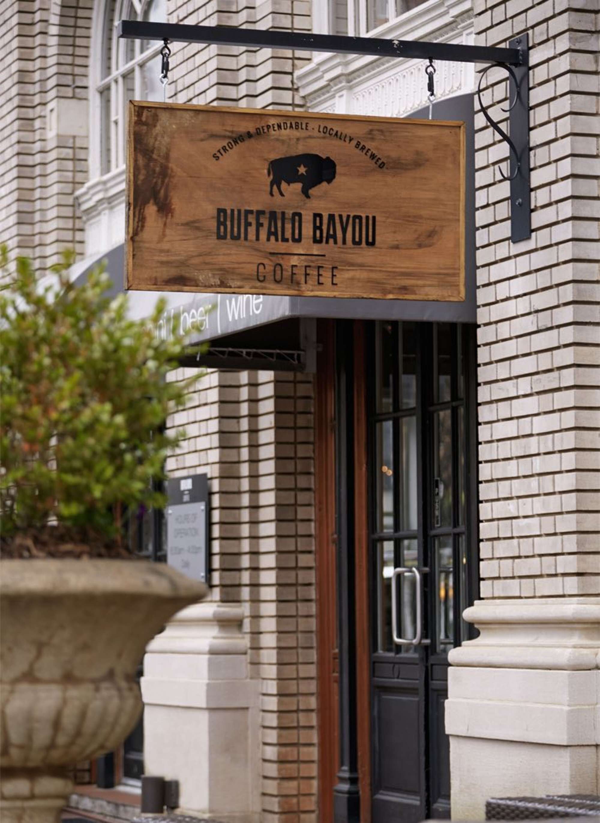 A wooden sign for Buffalo Bayou Coffee with a buffalo logo, hanging above a brick building entrance.