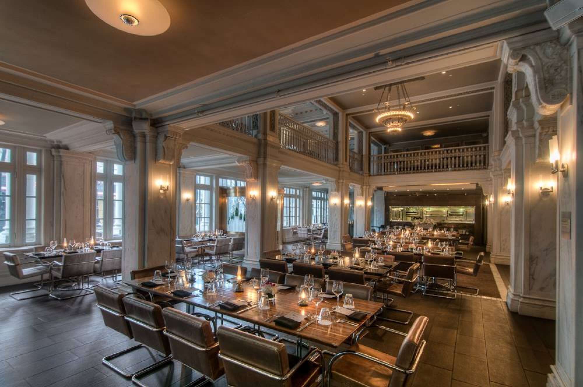 A spacious dining area with multiple tables, high ceilings, and large windows allowing natural light.