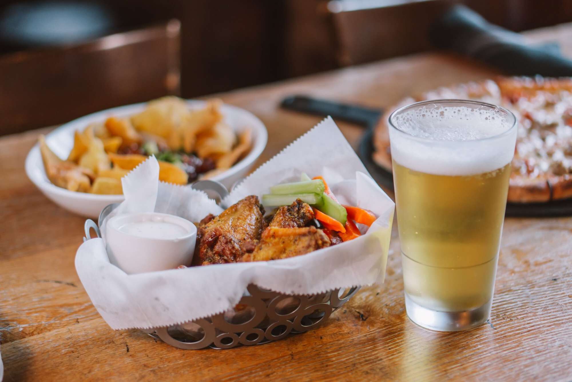A meal consisting of fried chicken, vegetables, and a side of fries, accompanied by a glass of beer on a wooden table.