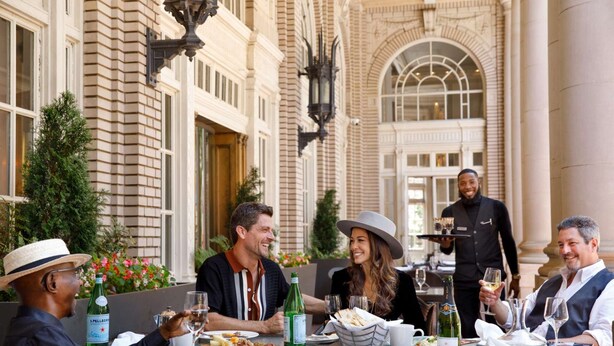 A group dining outdoors with a waiter, surrounded by a historic building with arched windows and a brick facade. - Fox Theatre Next Door | Rooftop Fitness + Dining (Atlanta)