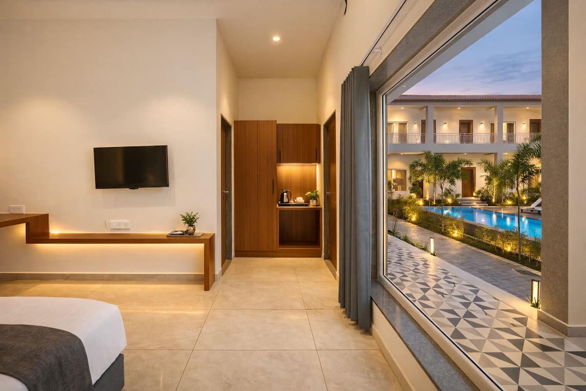 Une chambre d’hôtel équipée d’un lit, d’une télévision, d’un bureau, d’un petit coin cuisine et offrant une vue sur une piscine et un espace extérieur.