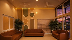 Een moderne lobby met een bruine leren bank, twee fauteuils, een plafondventilator en een groot raam met uitzicht op de zonsondergang.