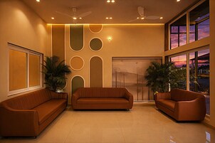 A modern lobby with a brown leather sofa, two armchairs, a ceiling fan, and a large window with a sunset view.