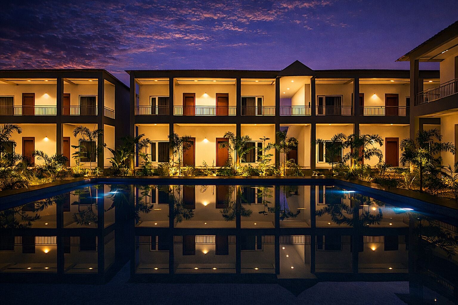 Un hôtel à plusieurs étages doté de balcons, d’une piscine et de plantes tropicales.