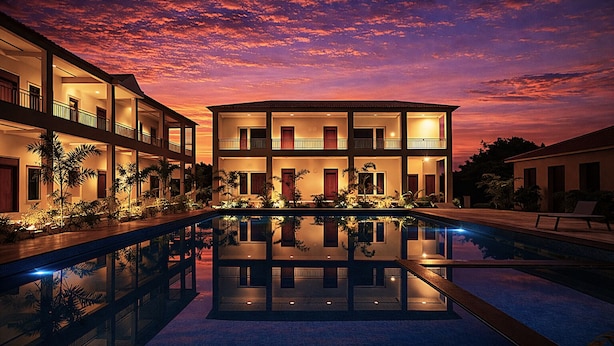 Een hotel met meerdere verdiepingen, met een zwembad dat de zonsondergang weerspiegelt.