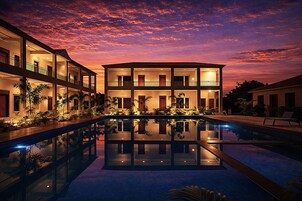 A multi-story hotel with a swimming pool reflecting the sunset.