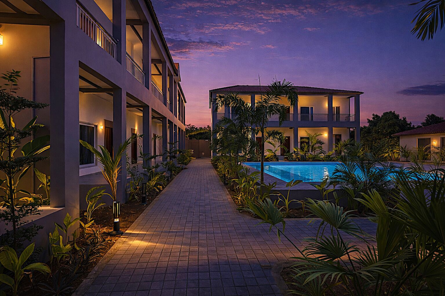 A modern hotel with a swimming pool, a covered outdoor area, and a pathway lined with plants.