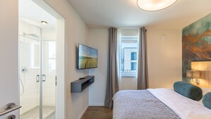 Ein Hotelzimmer mit Bett, Wandfernseher, Duschbereich und einem fenster mit Vorhängen.