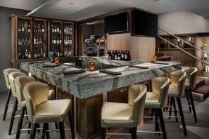 A bar area with a marble countertop, bar stools, and a wine display. - Near DC Monuments | Fitness Center + On-Site Dining (Arlington)