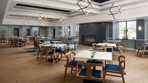A modern dining area with wooden tables and chairs, geometric pendant lights, and a fireplace. - Near Pimlico Race Course + Gym. Pickleball (Pikesville)