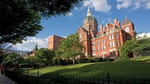 A large red brick building with a prominent dome and multiple towers, surrounded by well-maintained lawns and trees. - Close to Maryland Zoo in Baltimore + Dining & Gym (Pikesville)