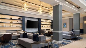 A modern lobby with a grey sofa set, a round coffee table, and a large flat-screen TV mounted on the wall.