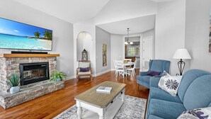 A spacious living room with a stone fireplace, a television mounted on the wall, and a dining area with a table and chairs. - L-8 Stunning views close to SDC (Branson)