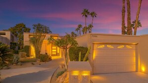 Ein modernes Haus mit Garage, Palmen und einer gut beleuchteten Auffahrt im Abenddämmerung.