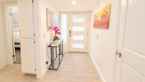Ein Flur mit weißen Wänden, Holzboden, einem Konsolentisch mit Blumentopf und einem Gemälde an der Wand.