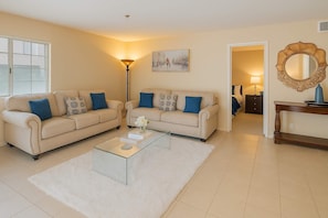 Una sala de estar con dos sofás color beige, una mesa de centro de vidrio y un tapete blanco.