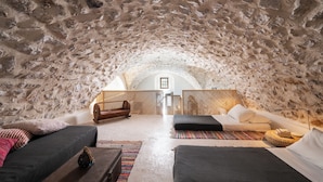 Een gezellige, rustieke kamer met een stenen plafond, een bed met een wit matras en kussens, een houten bank en een kleine tafel met een mand.