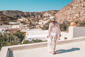 A person standing on a rooftop overlooking a village with white buildings and rocky hills. - Canava Villas Santorini (Santorini)