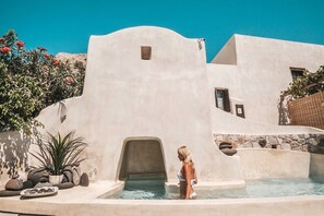 A modern building with a pool area, featuring a unique architectural design with a stone wall and a clear blue sky in the background. - Canava Villas Santorini (Santorini)