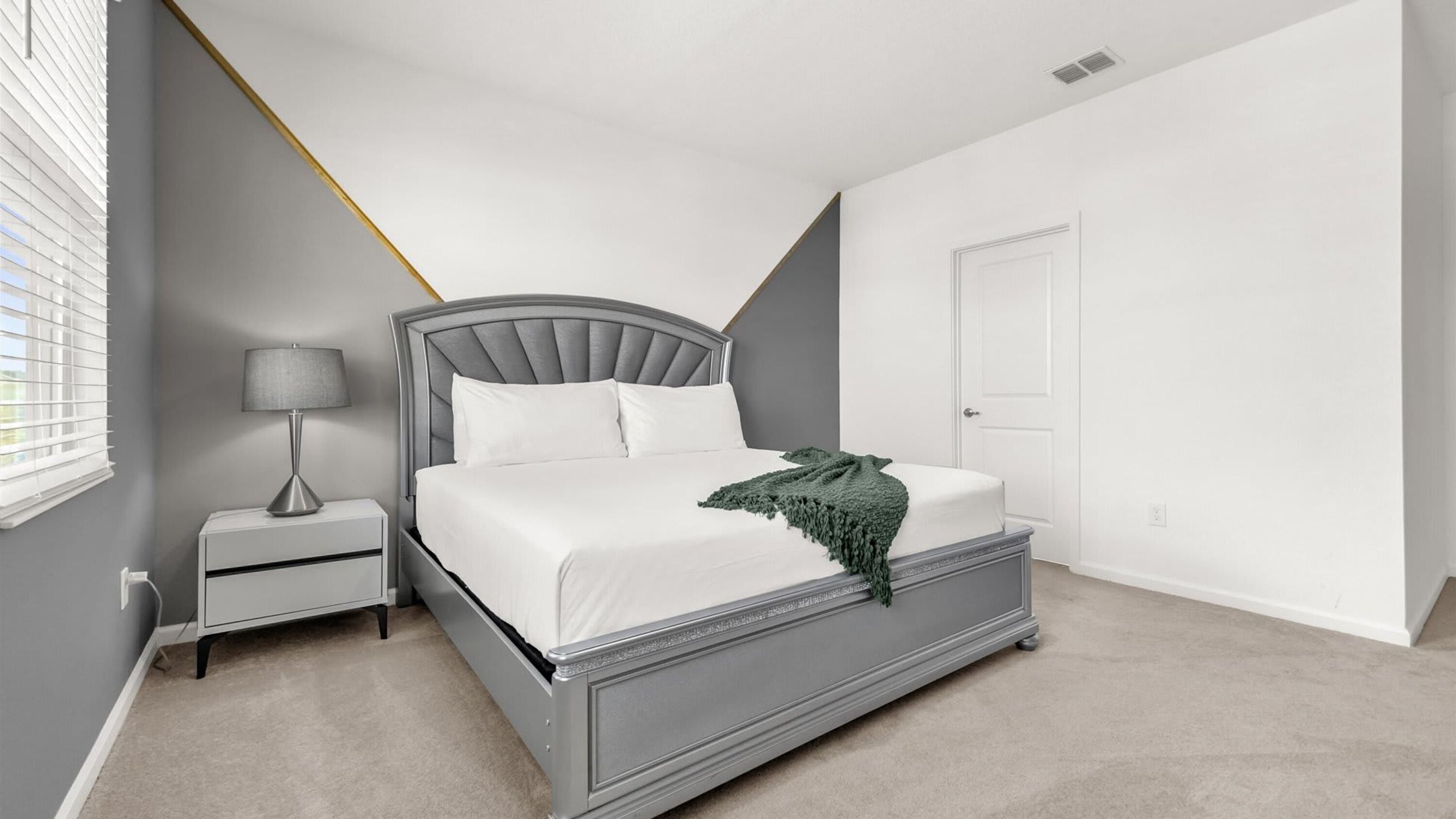A bedroom with a bed, nightstand, lamp, and a door.