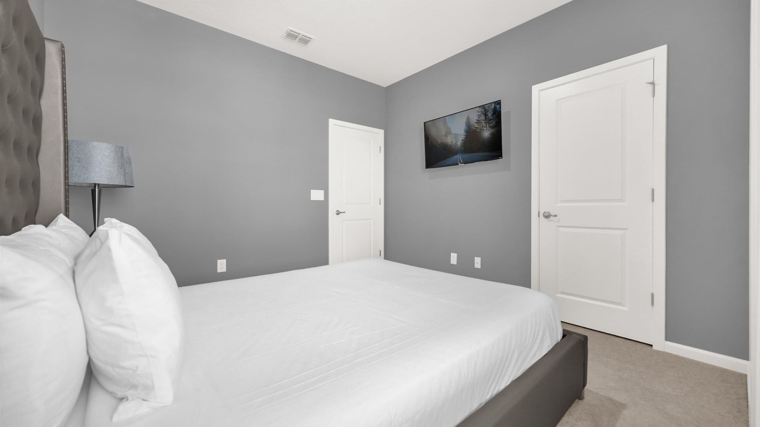 Un dormitorio con cama, dos puertas, un televisor de pared y una lámpara.