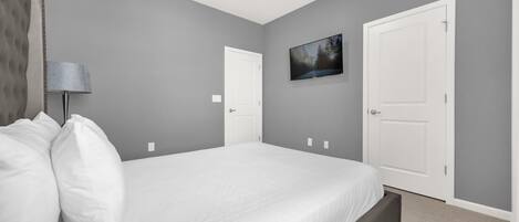 Un dormitorio con cama, dos puertas, un televisor de pared y una lámpara.