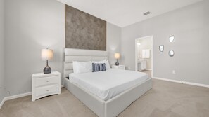 A modern bedroom with a large bed, two bedside tables with lamps, a large mirror, and a textured wall panel. - Upstay Spacious Villa w Pool Hot Tub Game Room (Kissimmee)