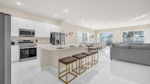 A modern kitchen with white cabinets, stainless steel appliances, and a central island with bar stools. - Upstay Spacious Villa w Pool Hot Tub Game Room (Kissimmee)