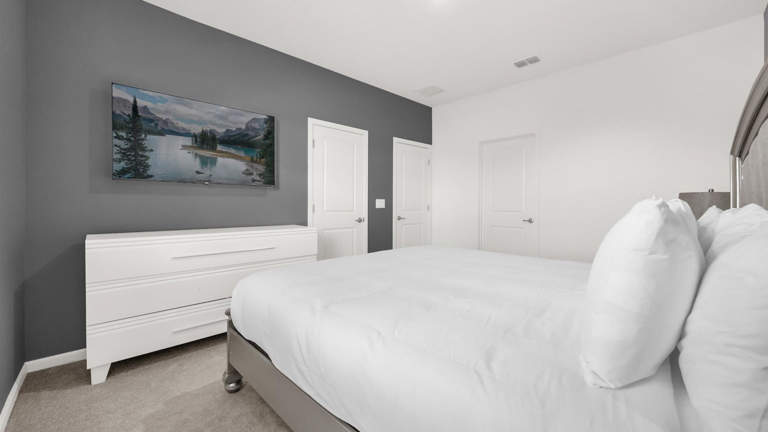 Une chambre à coucher avec un lit, une commode, un tableau et deux portes.