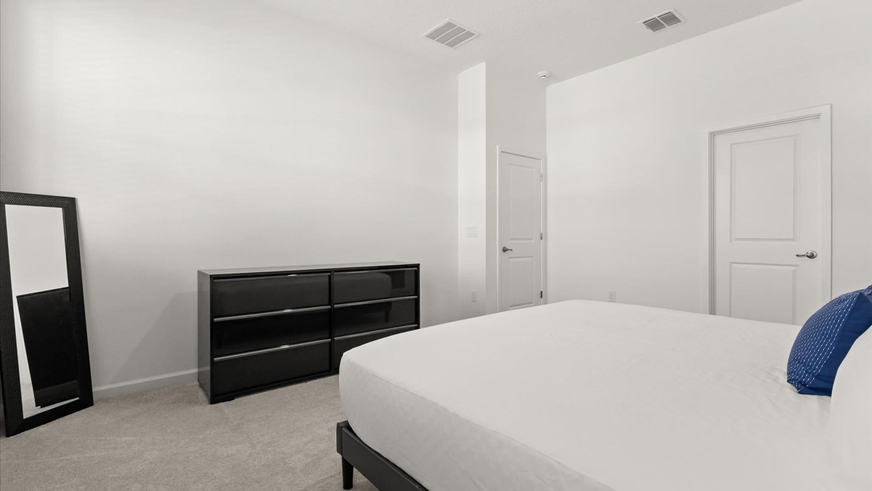 A bedroom with a bed, a black dresser, a white door, and a white wardrobe.